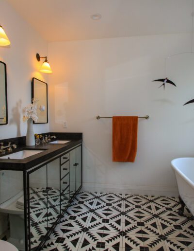 Modern bathroom interior with a glass shower, freestanding bathtub, patterned floor tiles, and a double vanity.