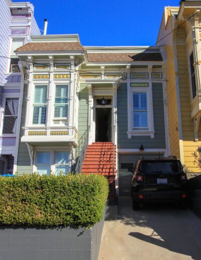 Classic victorian house with a staircase entrance and a parked car in front.