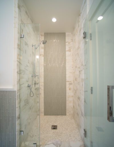 A modern bathroom with a glass-enclosed walk-in shower featuring marble tiles and a rain showerhead.