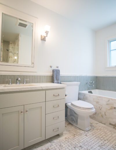 Modern bathroom with a floating vanity, tiled bathtub, and toilet by the window.