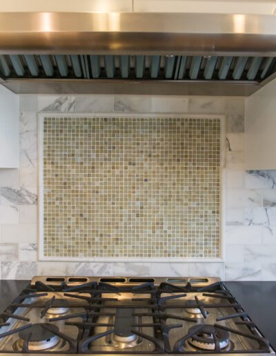 Stainless steel cooktop with gas burners, marble backsplash, and a modern range hood in a kitchen.