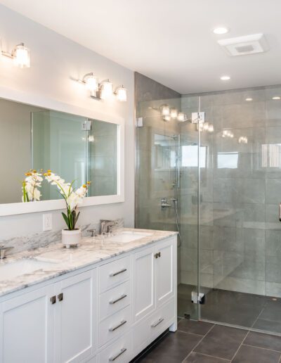 Modern bathroom interior featuring a large mirror, double vanity, and glass-enclosed shower area.