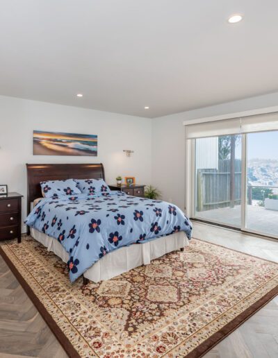 A spacious bedroom with a large bed, hardwood floors, and sliding glass doors leading to an outdoor area.