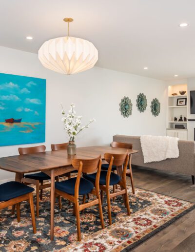 A bright, modern dining room with a wooden table and chairs, a large blue artwork on the wall, and a view of the city outside.