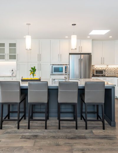 Modern kitchen interior with stainless steel appliances, white cabinetry, mosaic backsplash, and a central island with gray stools.
