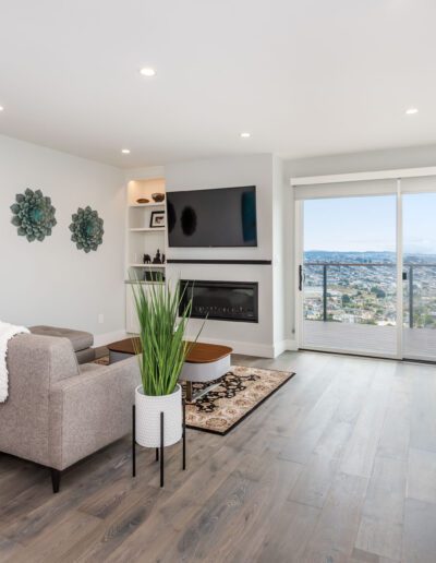 A modern living room with a sofa, mounted television, and a view of the outdoors through large windows.