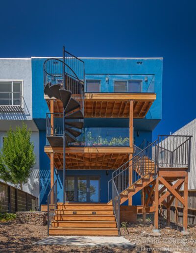 Modern blue residential building with wooden deck and spiral staircase.