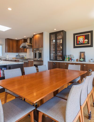 Modern kitchen with dining area featuring wooden furniture, stainless steel appliances, and ample natural light.