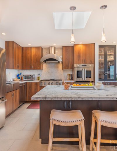 Modern kitchen interior with stainless steel appliances, wooden cabinetry, and a breakfast bar with stools.