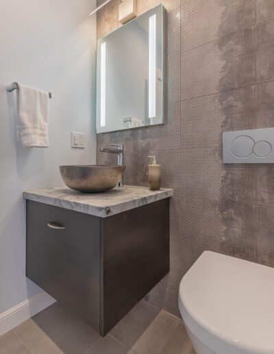 Modern bathroom with a wall-mounted vanity, vessel sink, and illuminated mirror.