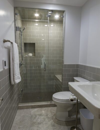 A modern bathroom with a walk-in shower, toilet, and sink, featuring gray tiles and clean lines.