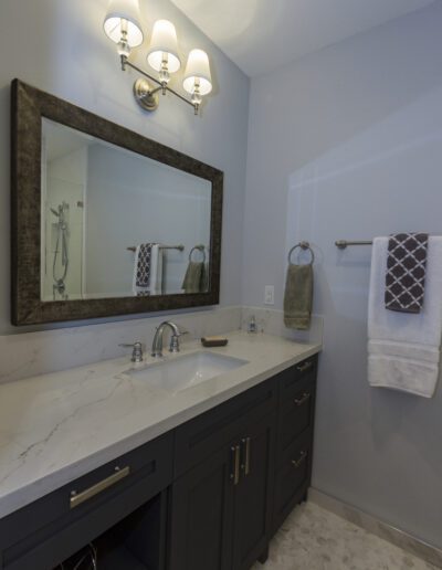 Modern bathroom interior with a granite countertop, double sink vanity, large mirror, wall-mounted towel holder, and a glass-enclosed shower area.