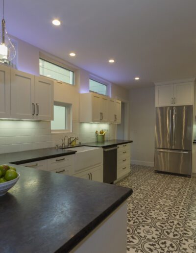 Modern kitchen interior with stainless steel appliances, white cabinets, and patterned floor tiles.