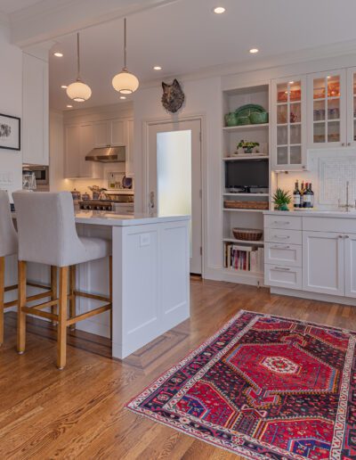 Modern kitchen with white cabinetry, stainless steel appliances, wooden floors, and a red area rug.