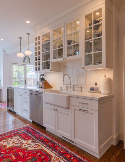 Bright kitchen interior with white cabinetry, wooden floors, and a well-organized open shelving unit.
