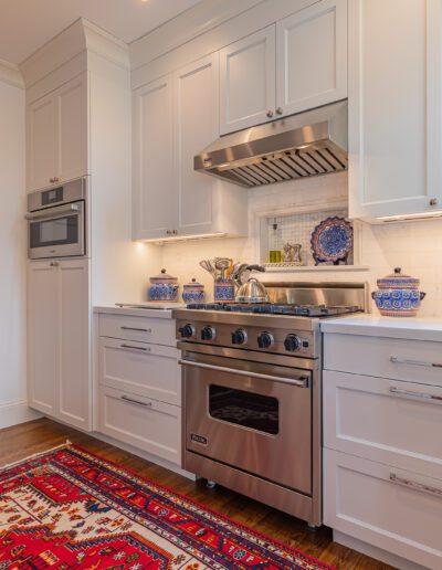 A modern kitchen with stainless steel appliances, white cabinetry, and a red oriental rug.