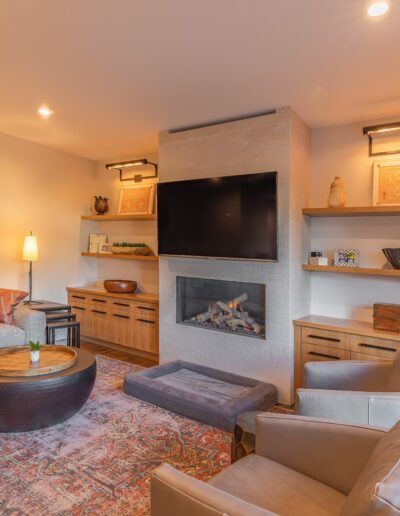 Modern living room with a sectional sofa, armchair, and ottoman, featuring a fireplace, built-in shelves with decor, and abstract wall art.