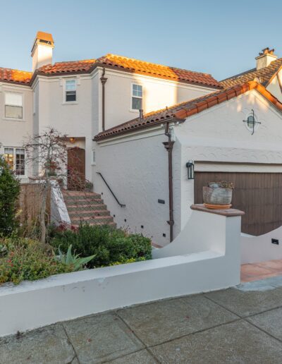 A traditional two-story house with a beige exterior, featuring a garage and a small front garden at sunset.